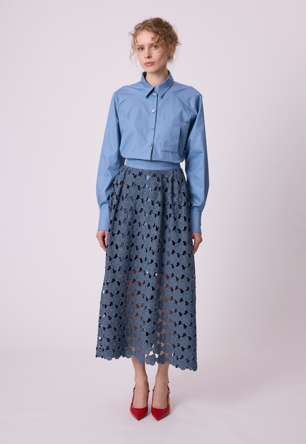Model wearing the blue Safira blouse in crisp cotton with tonal mother-of-pearl buttons and a floral lace skirt by Antonia Zander.